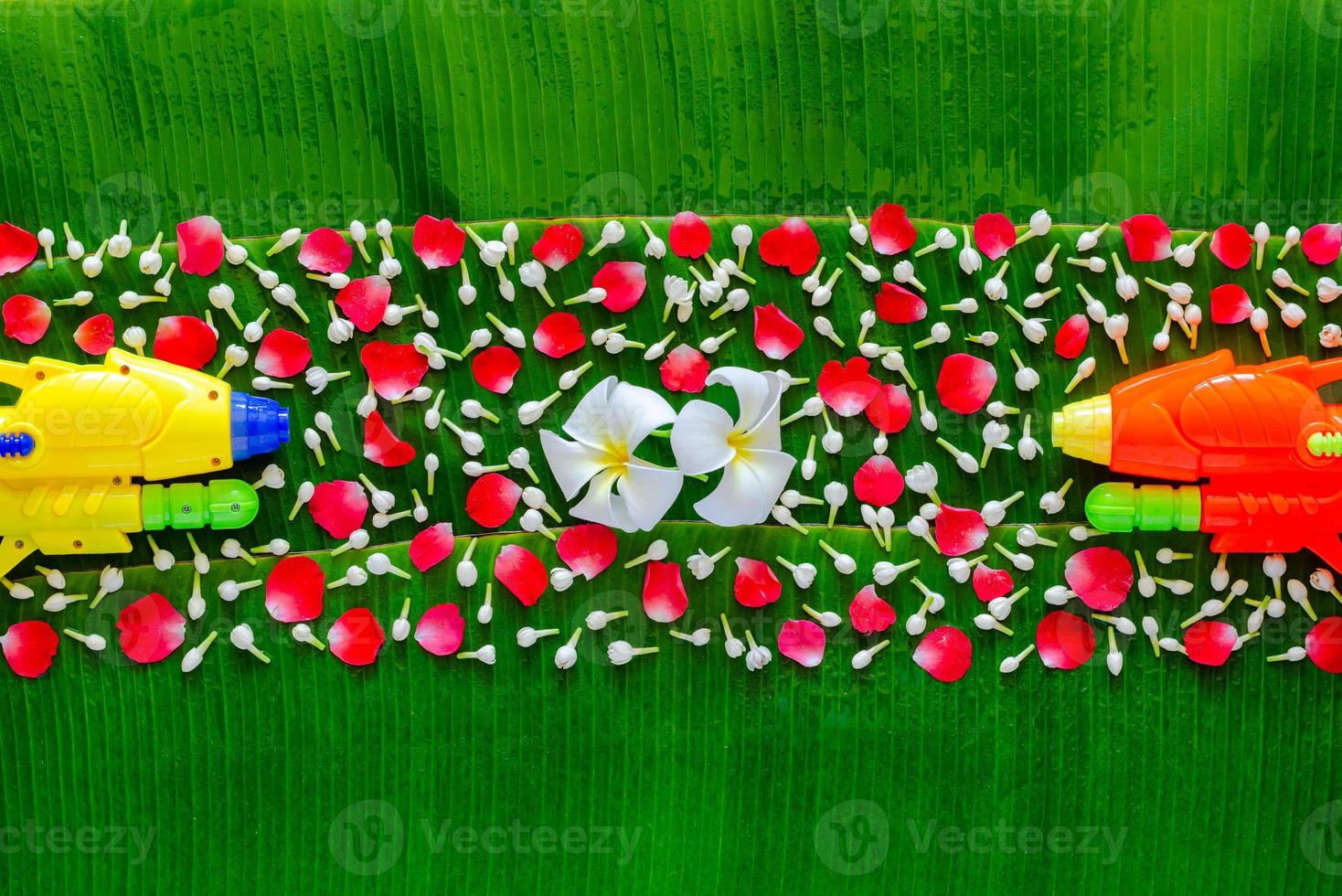 Songkran festival background with flowers and colorful water gun on wet banana leaf background. photo