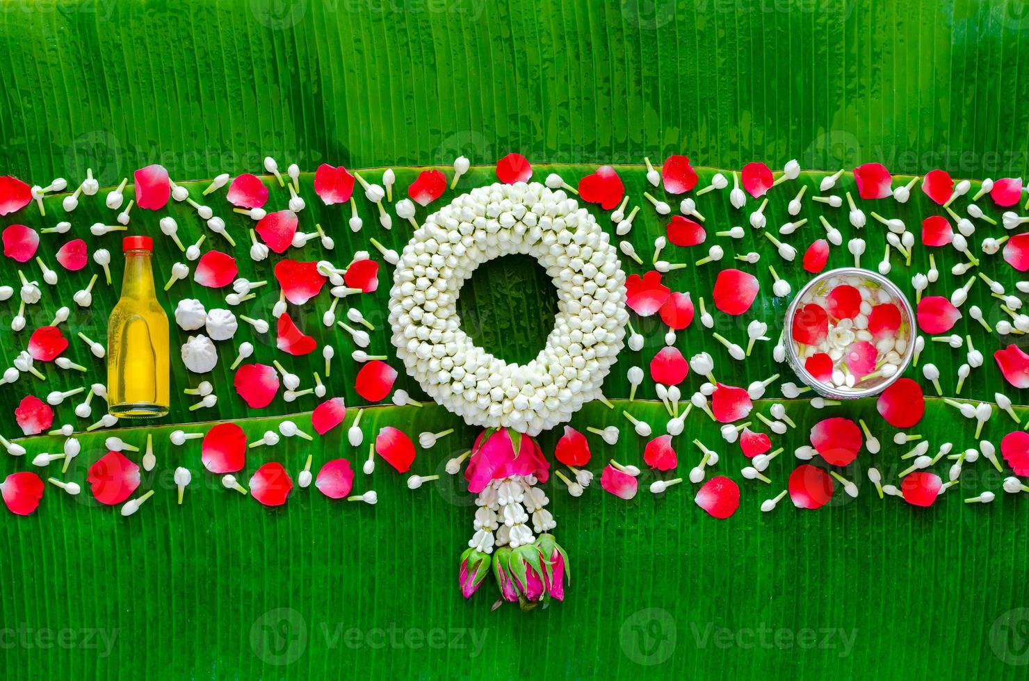 Songkran festival background with jasmine garland, flowers in water bowl, scented water and marly limestone for blessing on wet banana leaf background. photo