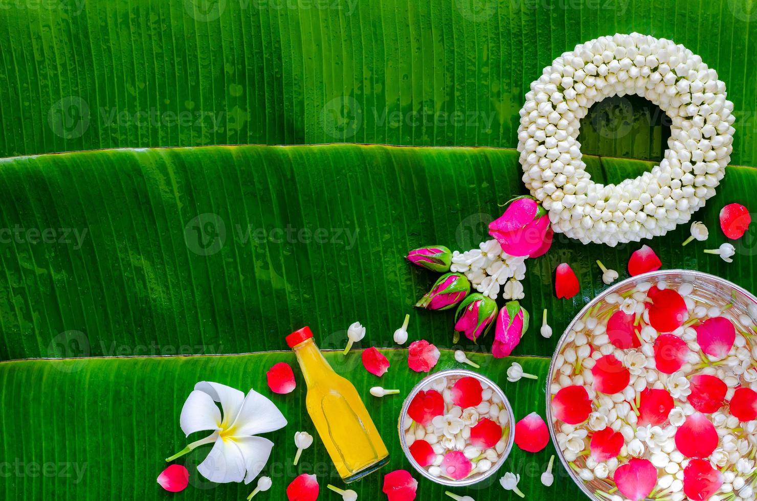 Songkran festival background with jasmine garland, flowers in water bowls and scented water for blessing on wet banana leaf background. photo