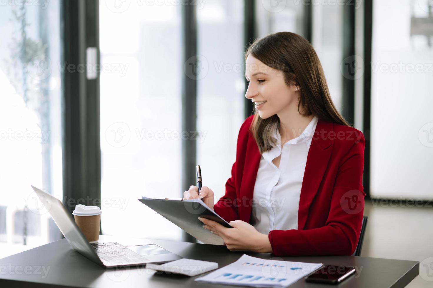 joven mujer hermosa escribiendo en una tableta y una computadora portátil mientras se sienta en la oficina moderna de la mesa de madera de trabajo foto