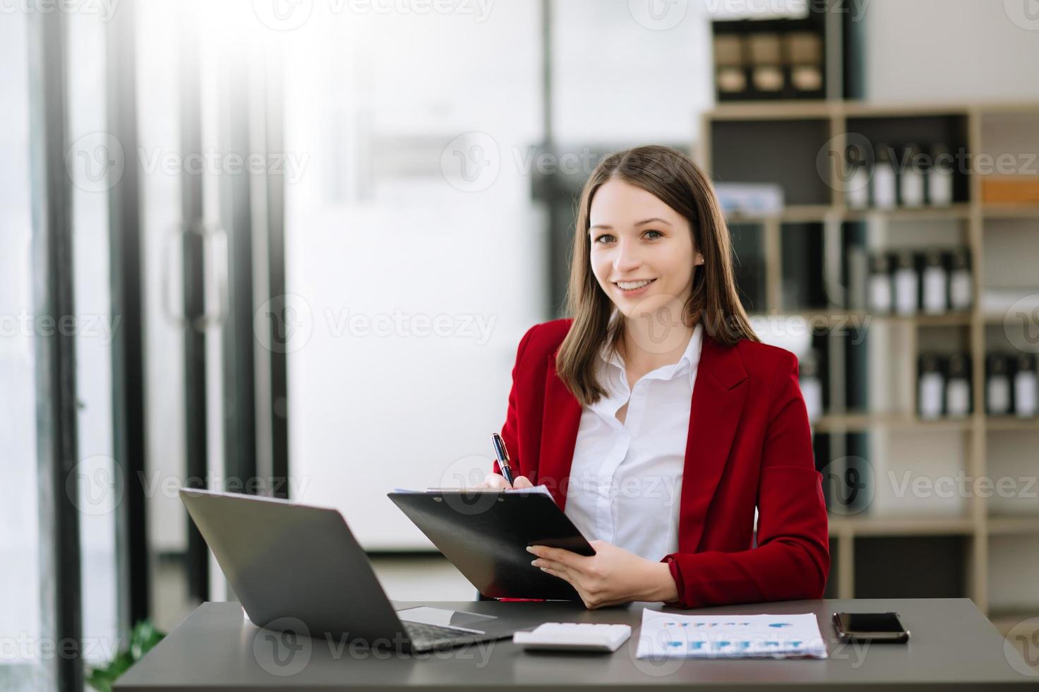 joven mujer hermosa escribiendo en una tableta y una computadora portátil mientras se sienta en la oficina moderna de la mesa de madera de trabajo foto