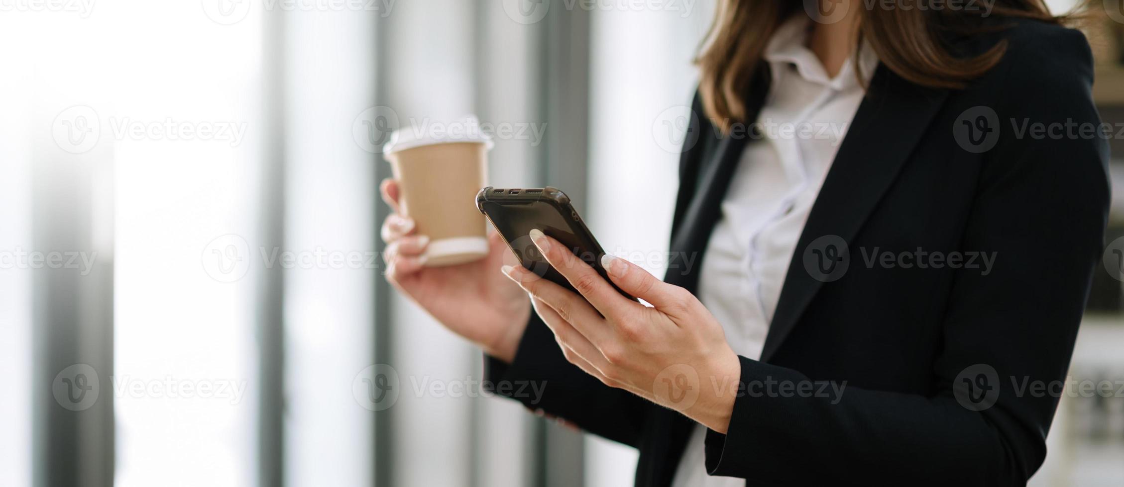 mujer usando una computadora portátil y escribiendo en una computadora portátil y sosteniendo una taza de café en la cafetería, oficina en casa a la luz de la mañana foto