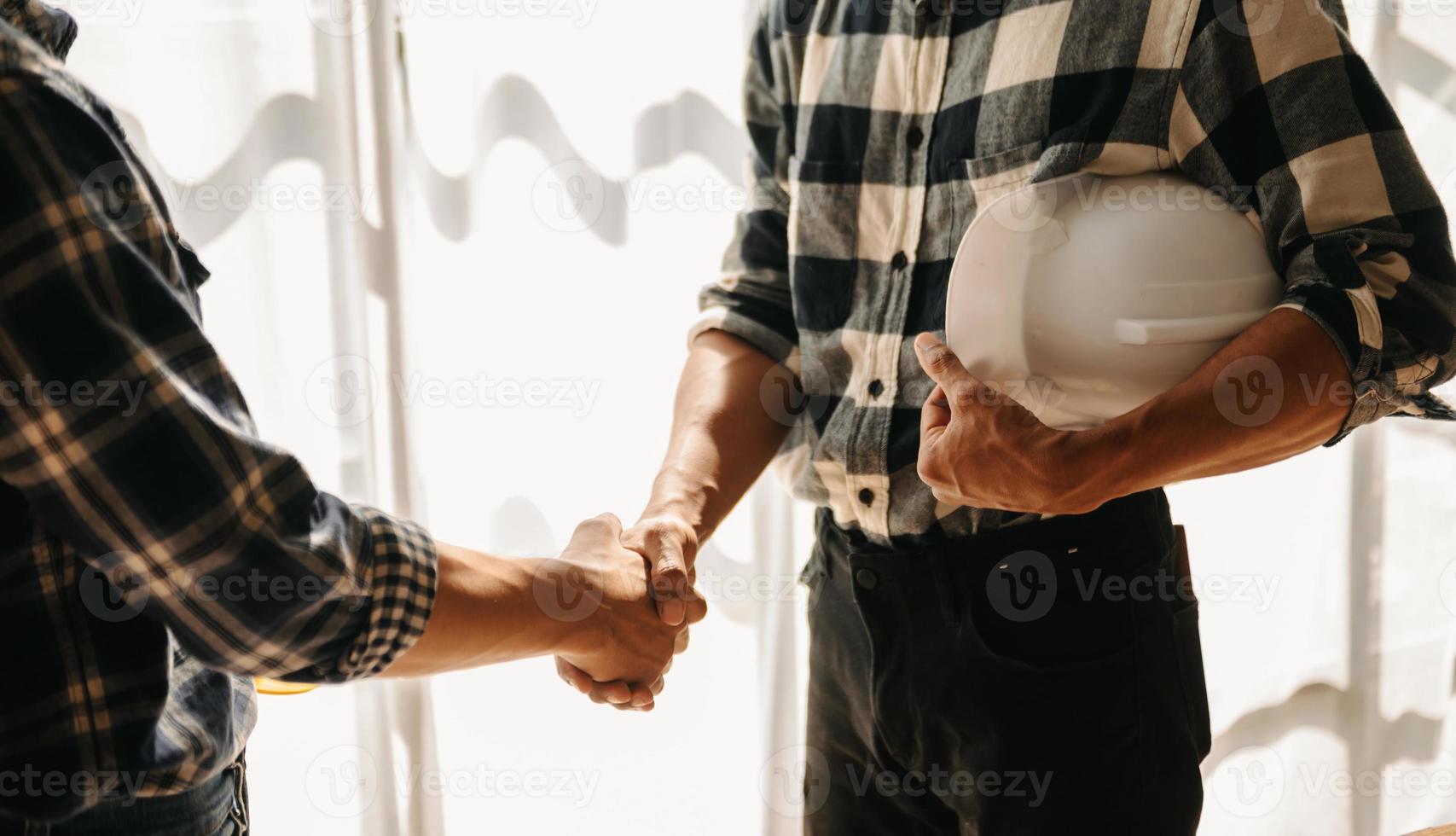 Engineers or architecture shaking hands at construction site for architectural project, holding safety helmet on their hands. photo