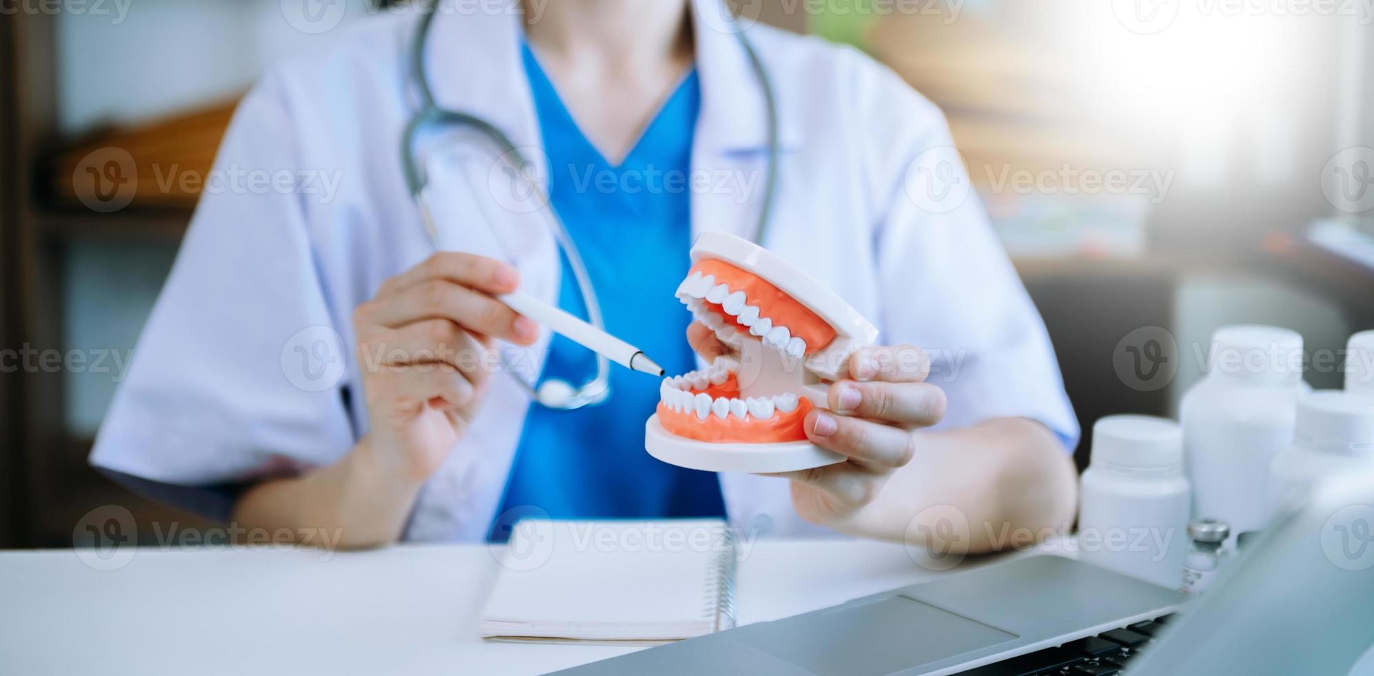 Concentrated dentist sitting at table with jaw samples tooth model and working with tablet and laptop in dental office professional dental clinic. photo