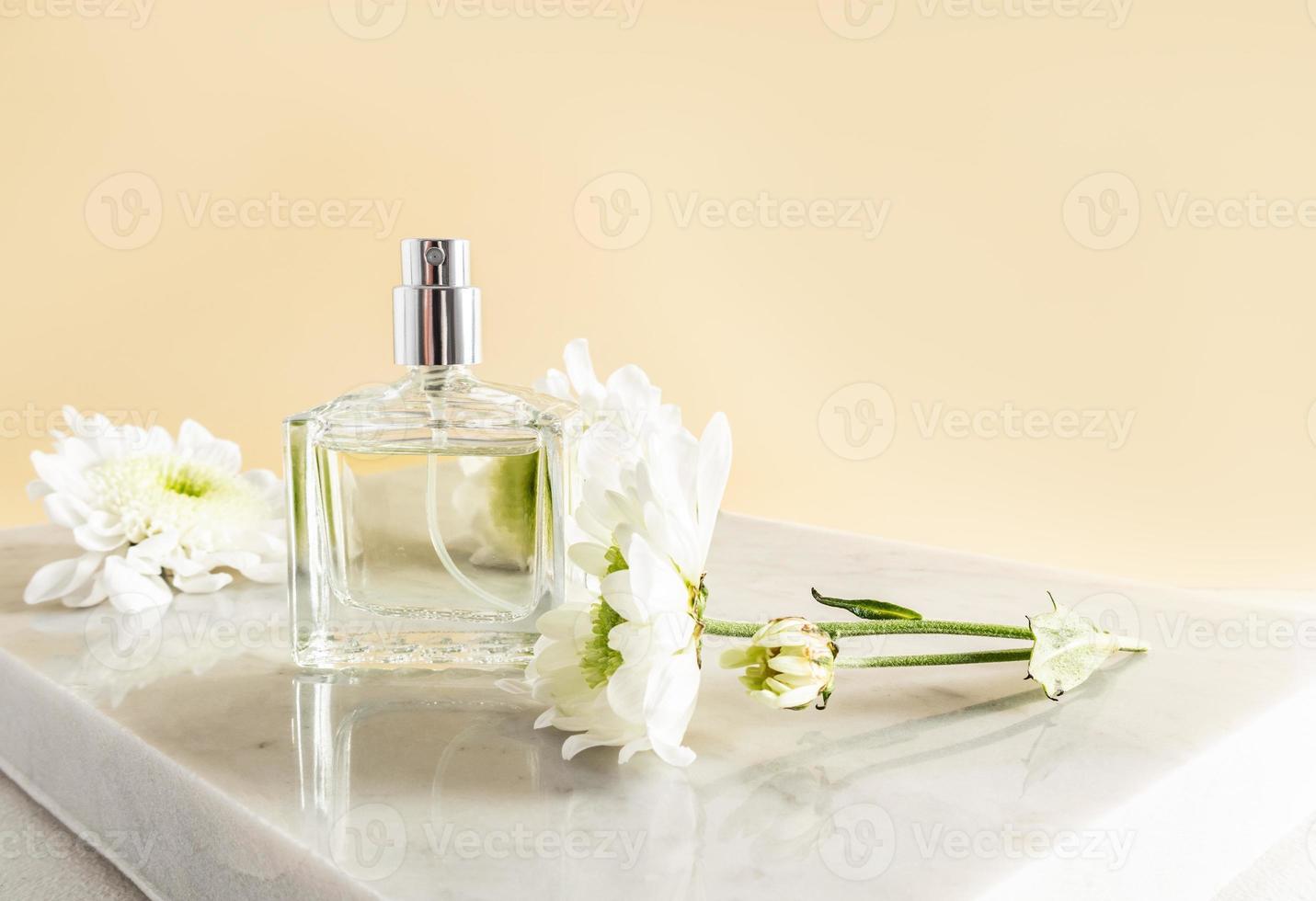 una botella transparente de perfume de mujer floral o agua de tocador en un podio de mármol con flores, fondo beige. presentación, publicidad de productos. foto