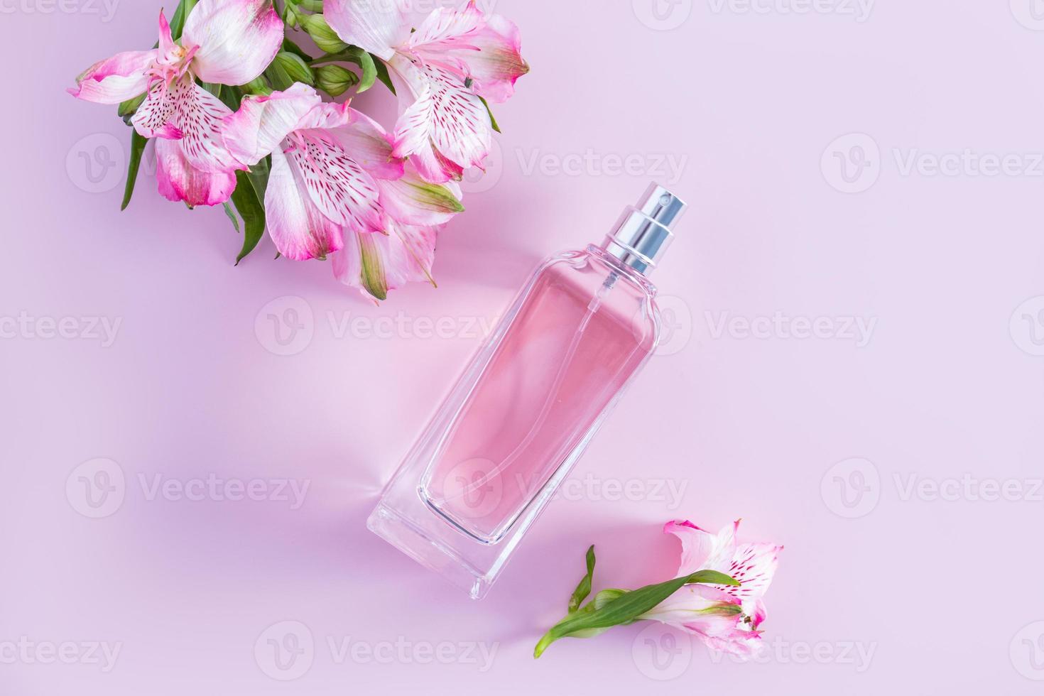aerosol de producto de perfume cosmético en una botella de vidrio sobre un fondo rosa con flores de primavera. vista superior. producto natural. foto