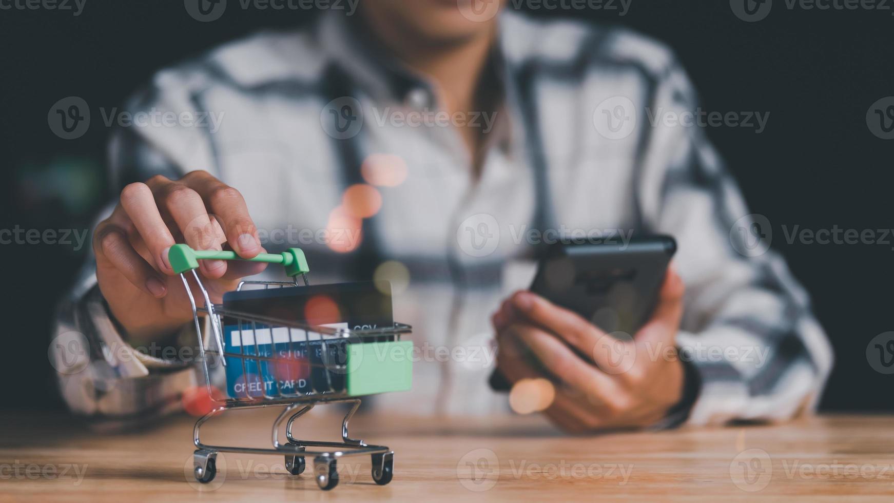 mano de hombre agarrando un carrito de compras, sociedad de consumo, concepto de adicción a las compras, servicio de compras en la web en línea y ofrece entrega a domicilio, conectando comerciantes y clientes de todo el mundo, pago en línea foto