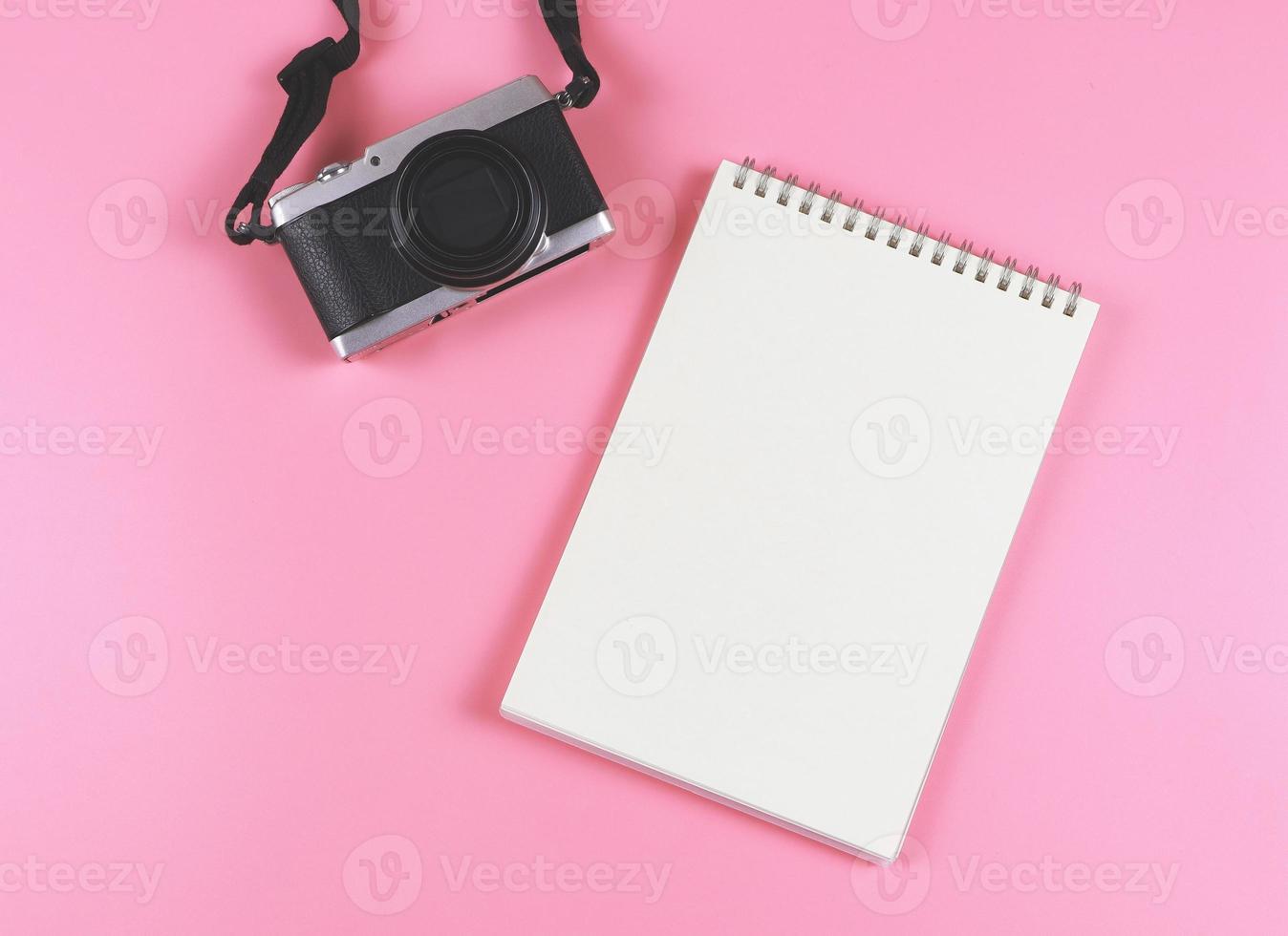 endecha plana de cuaderno abierto de página en blanco y cámara sobre fondo rosa. foto