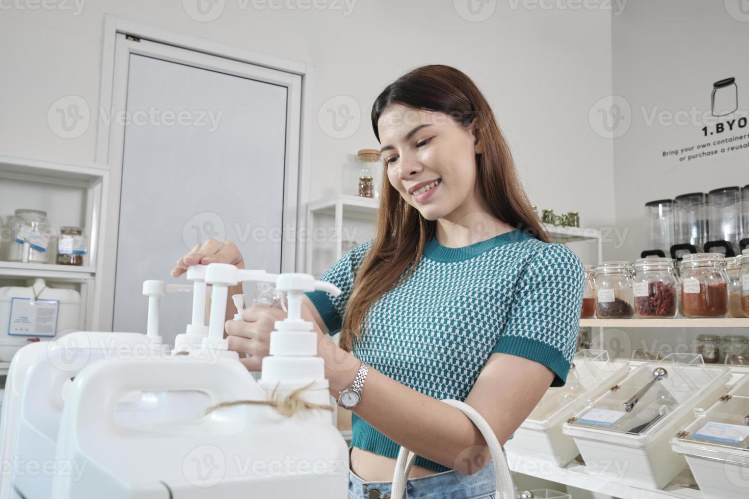 A Caucasian female customer pressed a reusable container to fill liquid products to recycle bottles at zero-waste and refill store, environment-friendly groceries, and sustainable shopping lifestyle. photo