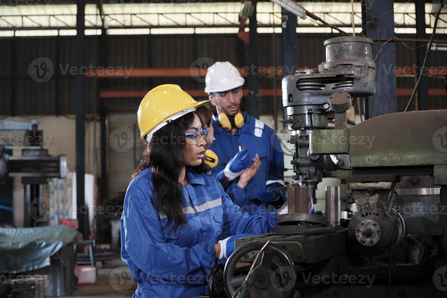 un equipo de trabajadores industriales con uniformes de protección y seguridad y cascos, un gerente masculino y colegas femeninas trabajan con máquinas de metalurgia en la fábrica de fabricación. ingeniero de producción profesional. foto