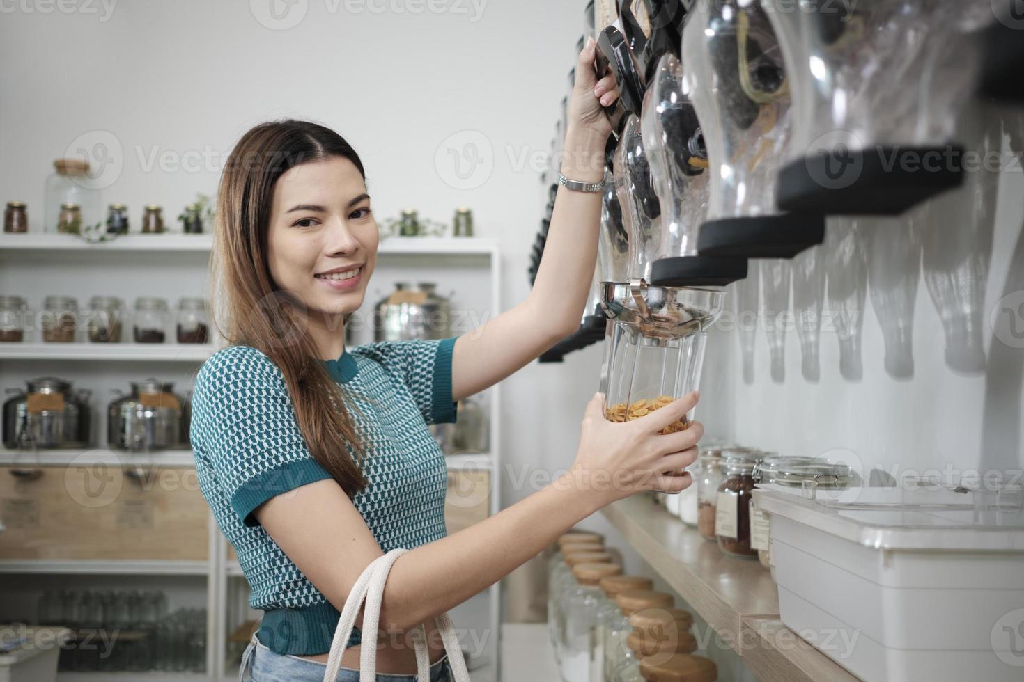 A Caucasian female customer fills cereal foods in a glass jar, lever the reusable container on refill store shelves, zero-waste and plastic-free grocery, environment-friendly, sustainable lifestyles. photo