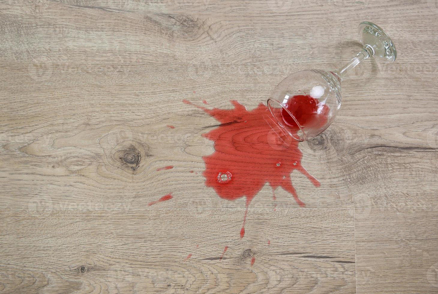 Glass of red wine fell on laminate, wine spilled on floor. photo