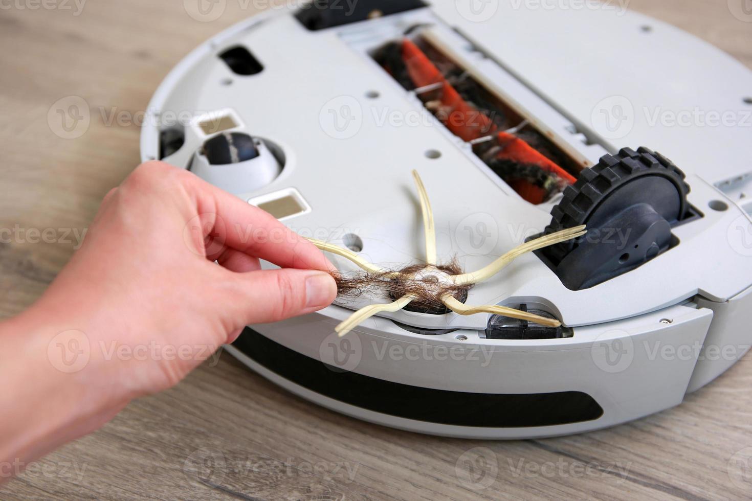 A woman  removes hair from the brush of a robot vacuum cleaner. The concept of a robot vacuum cleaner cleans the floors in the house. photo