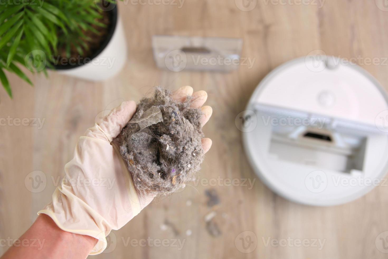 A woman holds a dust collector with garbage. The concept of a robot vacuum cleaner cleans the floors in the house. photo