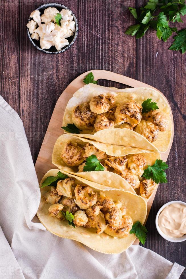 Grilled cauliflower tacos with herbs on a board on the table. Vegetarian food. Top and vertical view photo