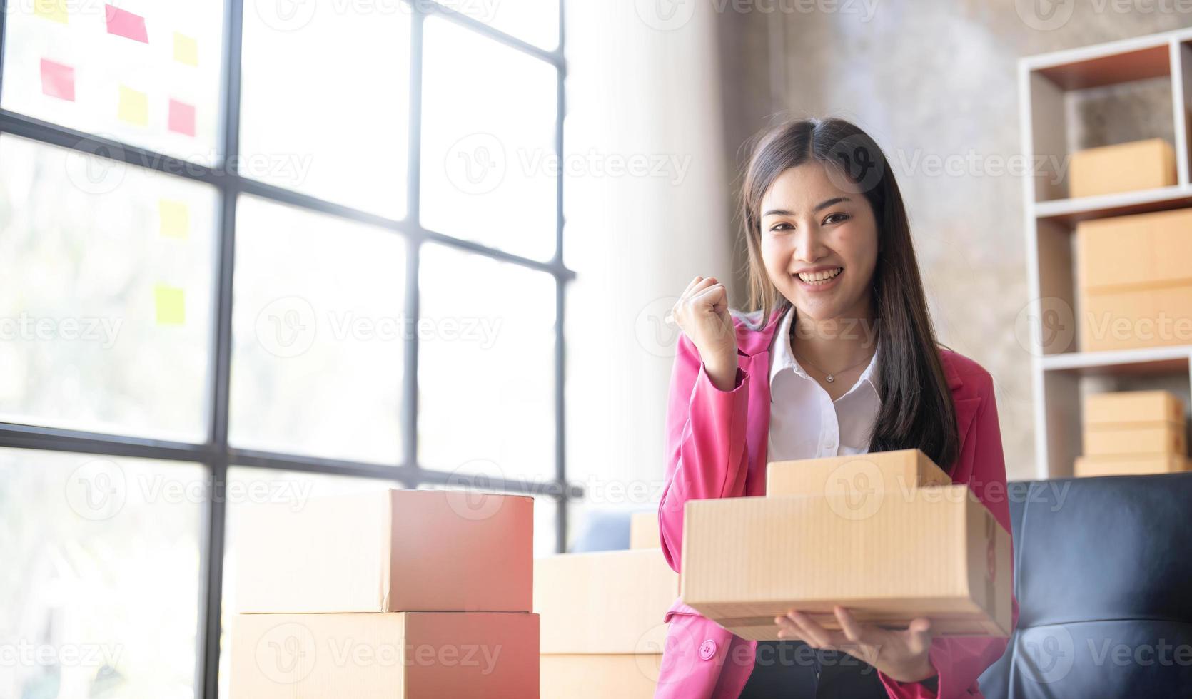 Startup SME small business entrepreneur of freelance Asian woman using a laptop with box Cheerful success happy Asian woman her hand lifts up online marketing packaging and delivery SME idea concept photo