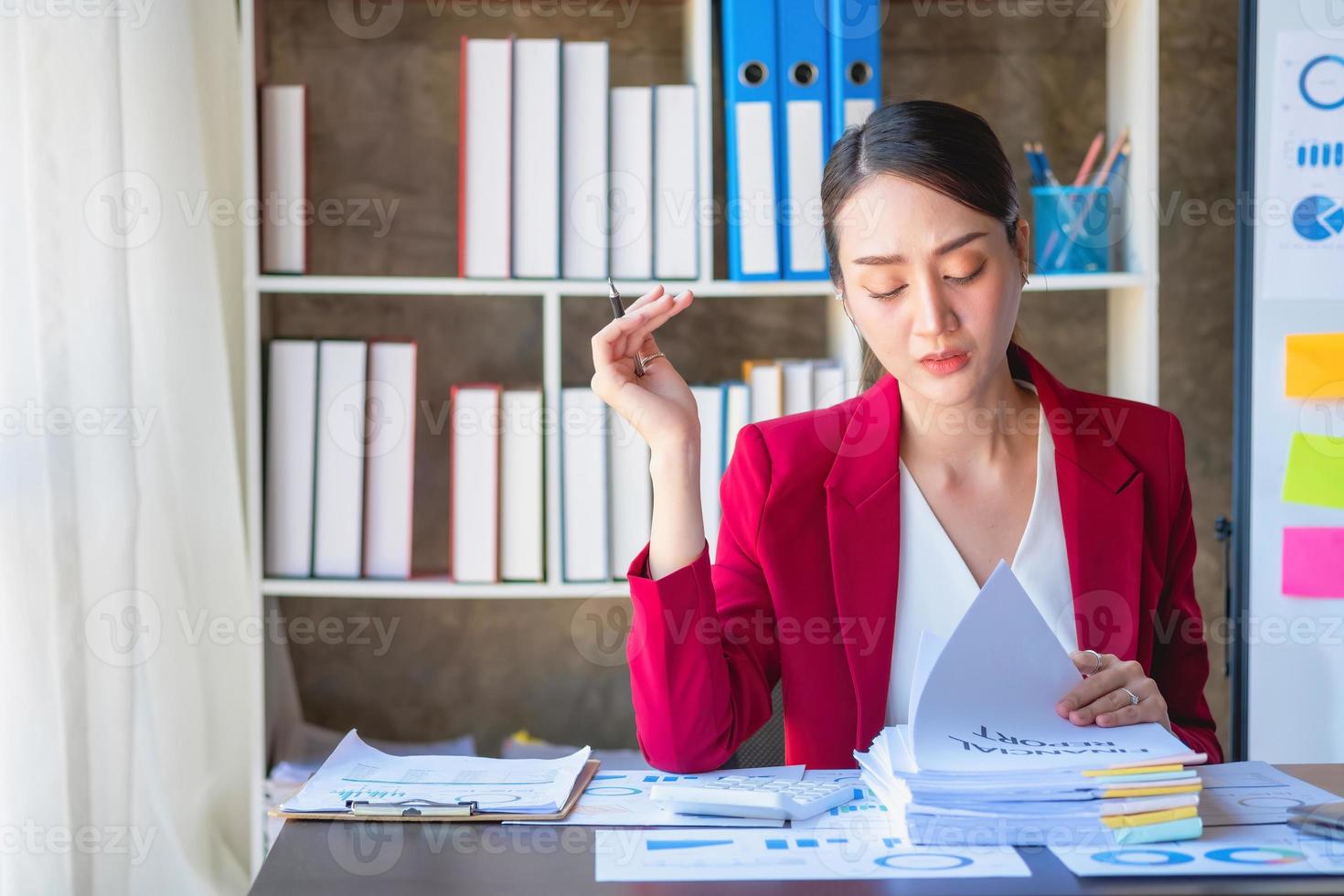 financiera, mujer de negocios asiática con traje rojo sosteniendo una taza de café sentada en el escritorio de la oficina, teniendo una computadora para hacer trabajo de contabilidad en el lugar de trabajo para calcular el beneficio anual por deber, idea de negocio foto