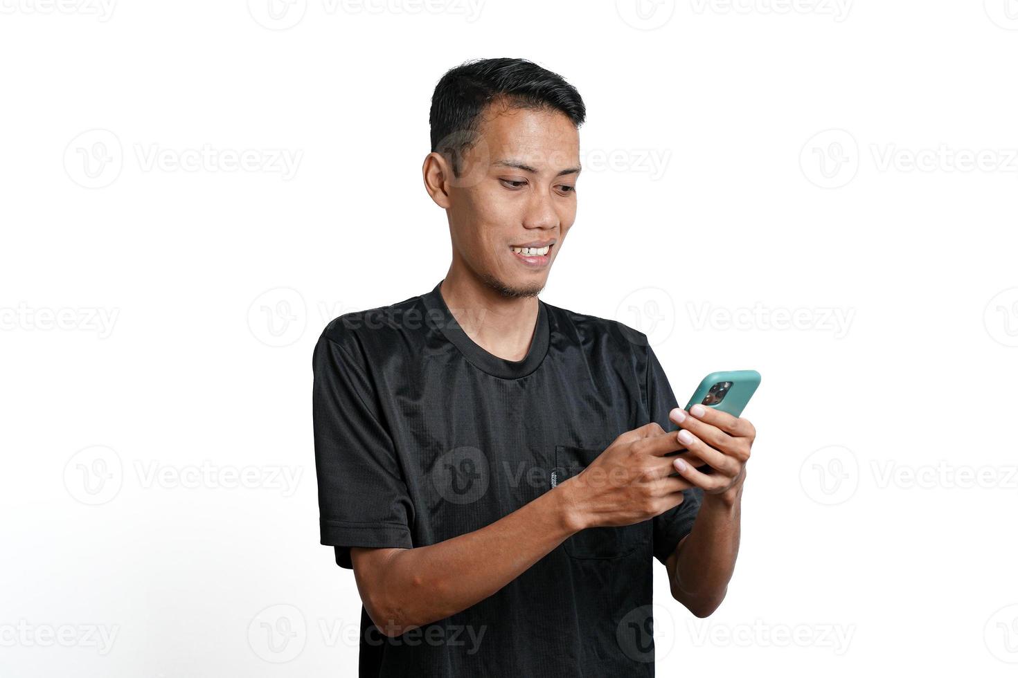 Asian man wearing black training t-shirt, With a happy excited gesture while looking at the smartphone screen. Isolated by white background photo