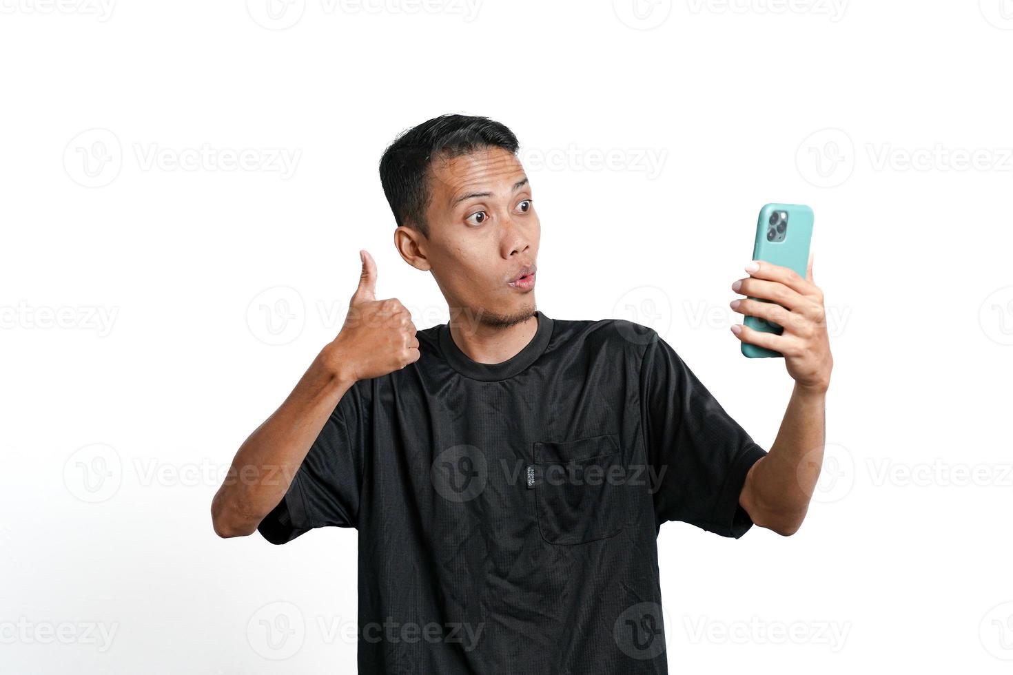 Asian man wearing black training t-shirt, With a happy excited gesture while looking at the smartphone screen. Isolated by white background photo