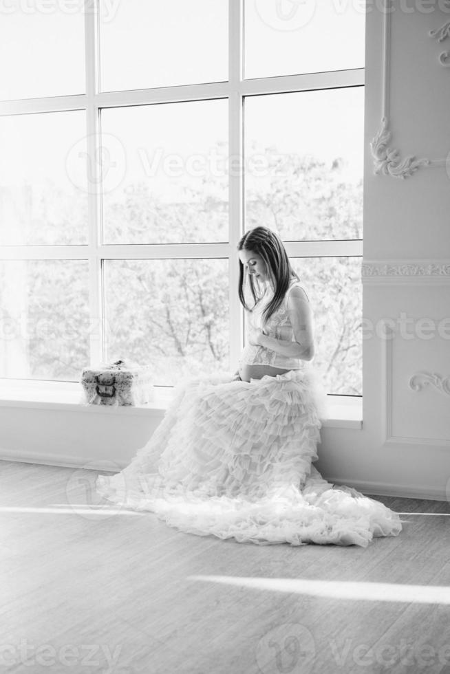 red-haired pregnant young girl in a white dress near the window photo