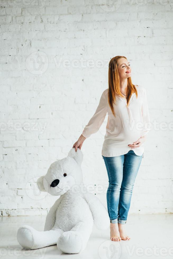 red-haired pregnant girl in a light blouse and blue jeans with a teddy bear photo