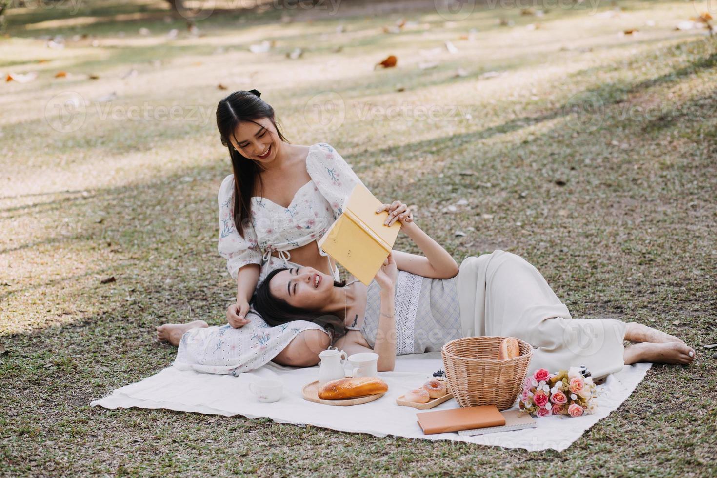 Young pretty brunette twin girls sitting on the grass with legs slightly bent in knees and looking in a brown book, wearing casual coat in autumn sunny weather on blurry background. photo