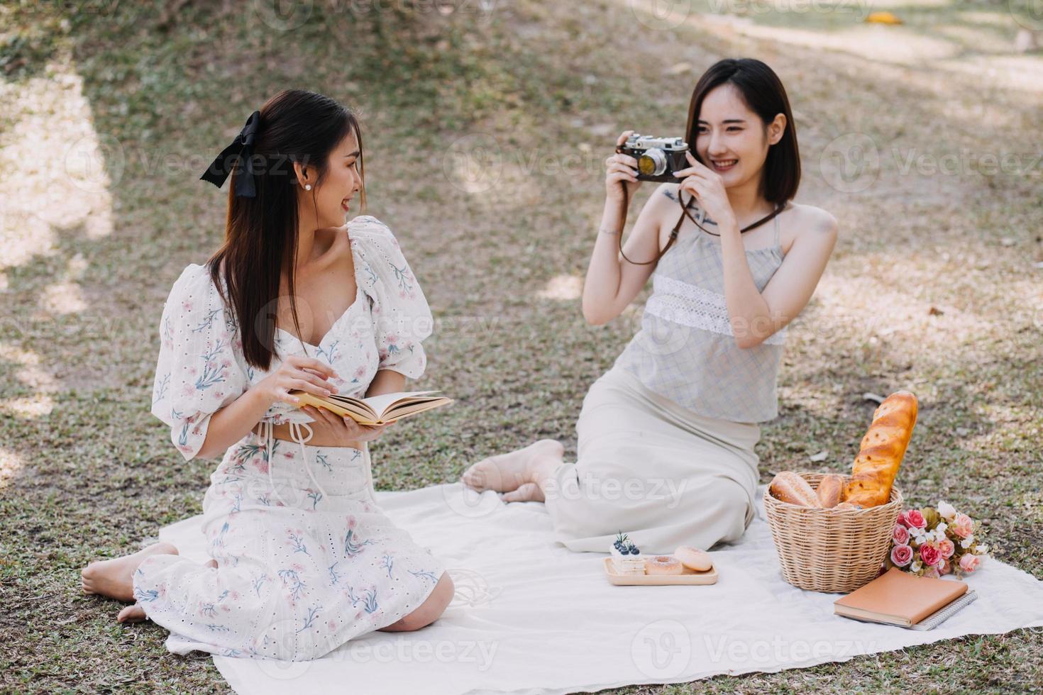Young pretty brunette twin girls sitting on the grass with legs slightly bent in knees and looking in a brown book, wearing casual coat in autumn sunny weather on blurry background. photo