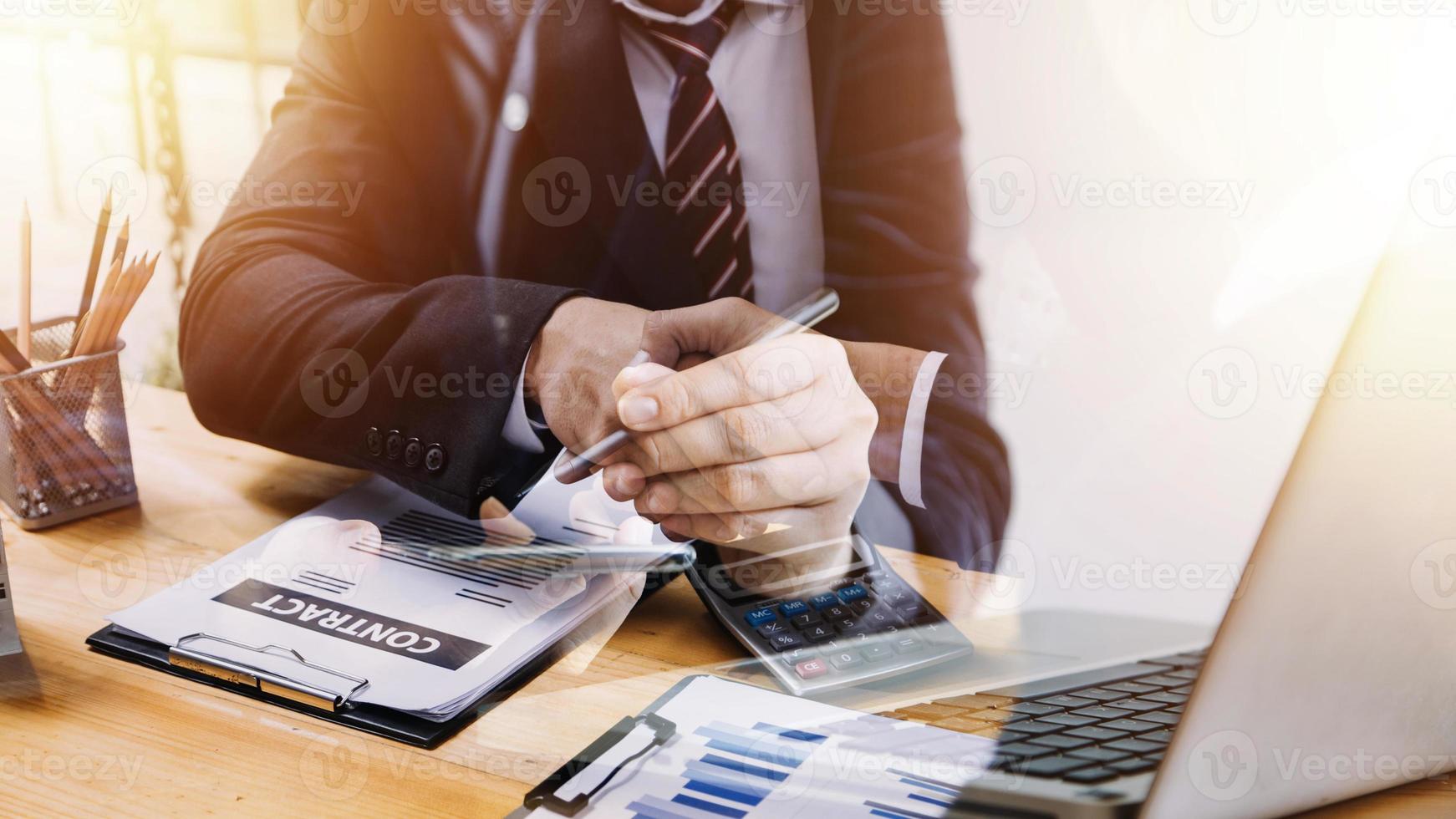 Multi-tasking businessman working in the office. He is using touchpad while reading an e-mail on laptop and taking notes on the paper. photo