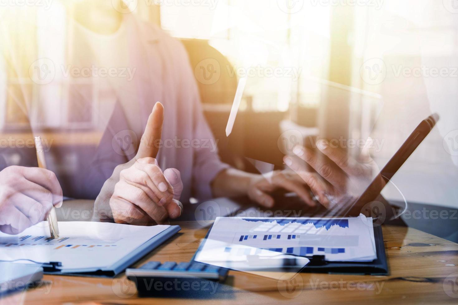 Multi-tasking businessman working in the office. He is using touchpad while reading an e-mail on laptop and taking notes on the paper. photo
