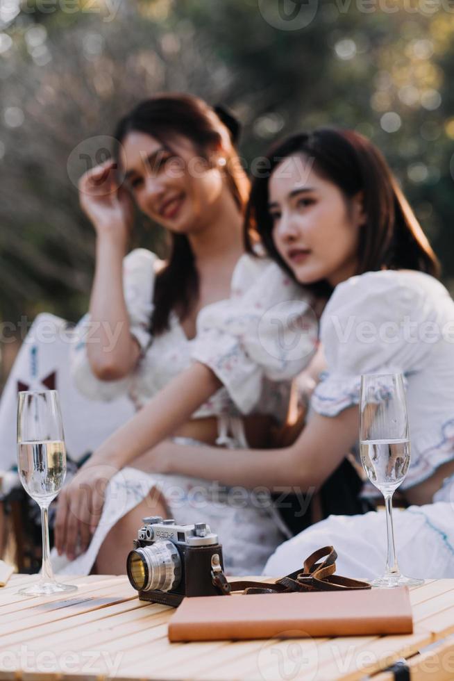 Young pretty brunette twin girls sitting on the grass with legs slightly bent in knees and looking in a brown book, wearing casual coat in autumn sunny weather on blurry background. photo
