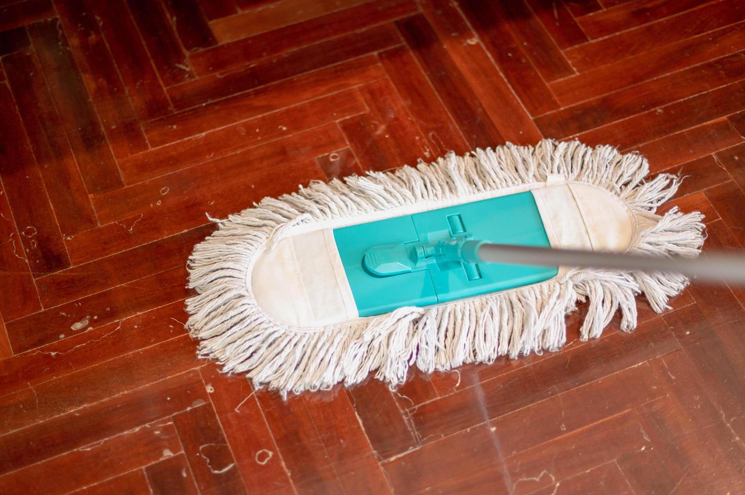 mano femenina con guantes protectores usando un trapeador húmedo plano mientras limpia el piso de la casa. foto
