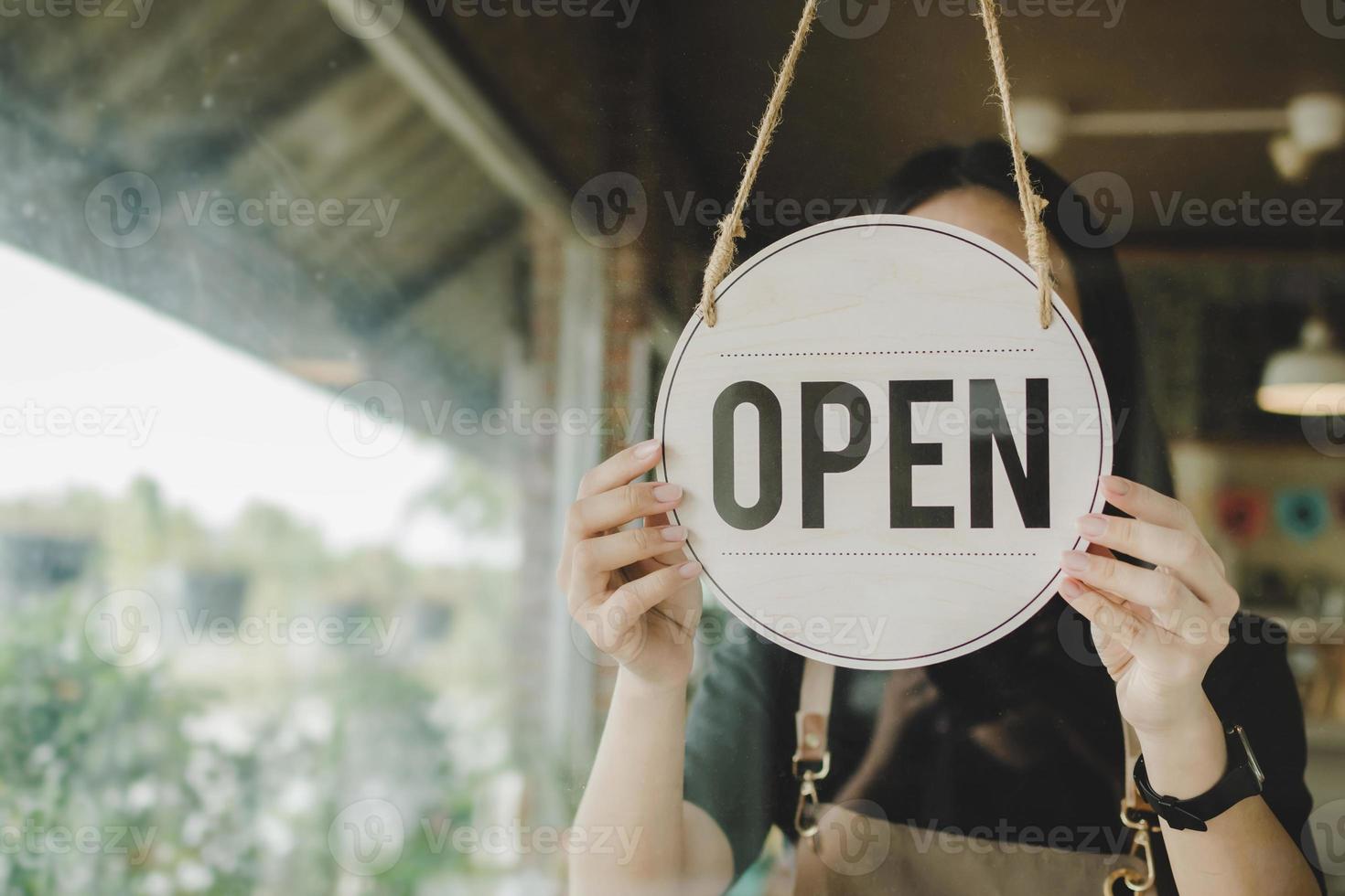 young asian staff woman wearing protection face mask turning open sign board on glass door in modern cafe coffee shop, hotel service, cafe restaurant, retail store, small business owner concept photo