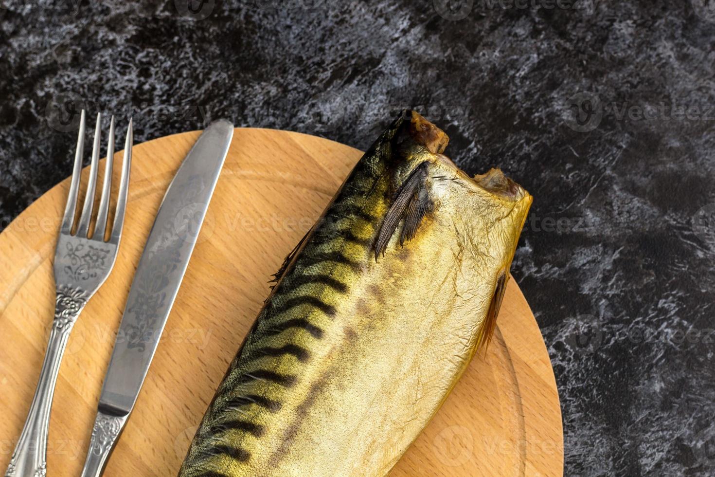Smoked mackerel without head with fork knife cutting board on black background photo