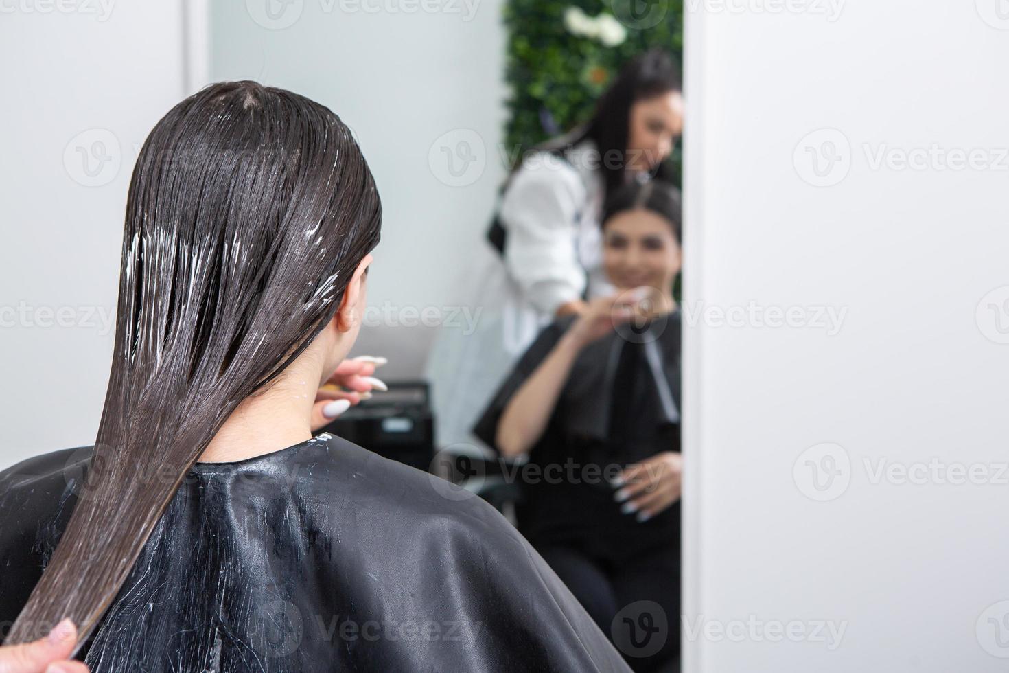 el peluquero aplica una máscara para el cabello al cabello negro liso. cuidado del cabello en el salón de belleza. foto