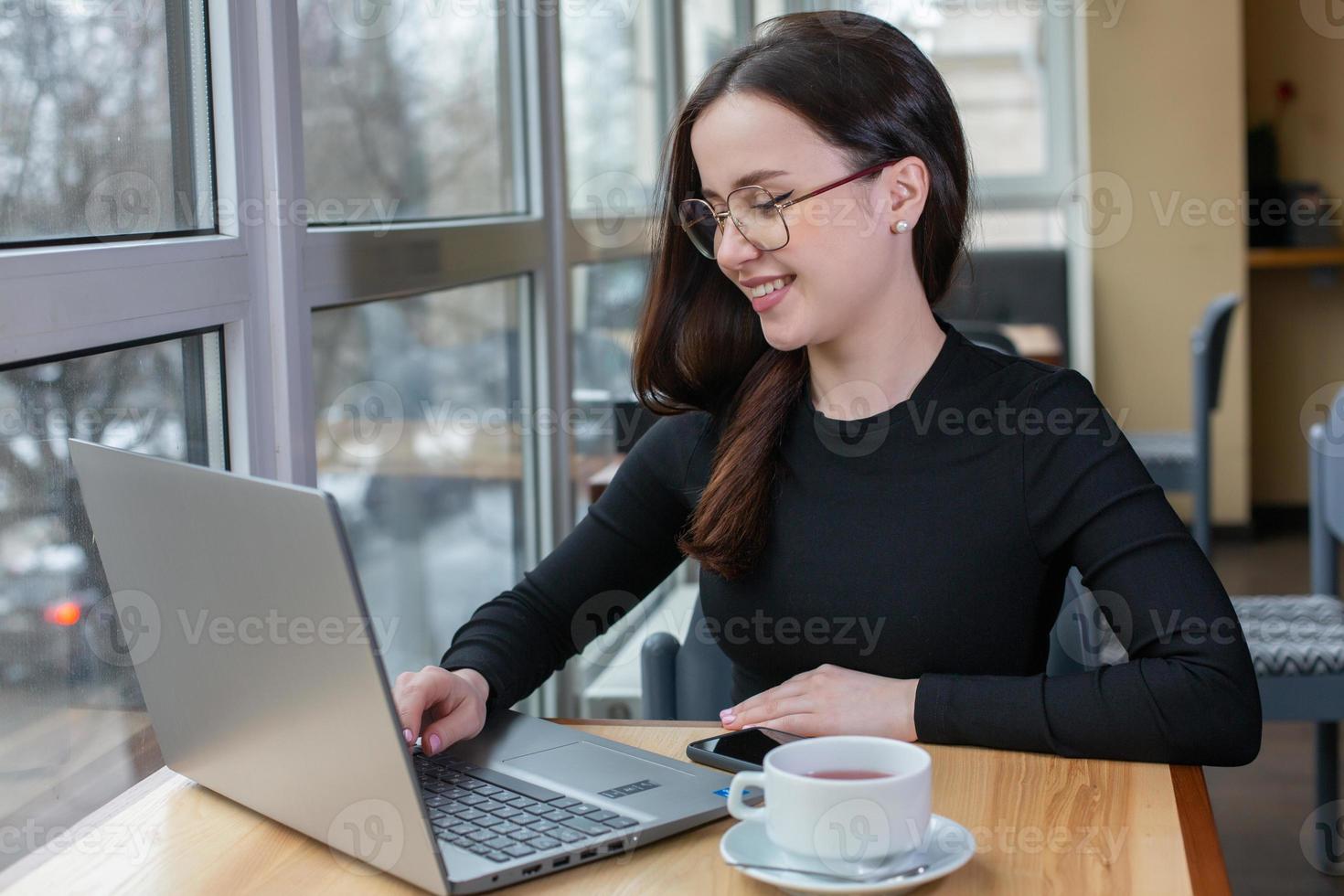 bella mujer de negocios trabajando en una laptop en una cafetería. mujer independiente que se conecta a internet a través de la computadora. blogger o periodista escribiendo un nuevo artículo. foto