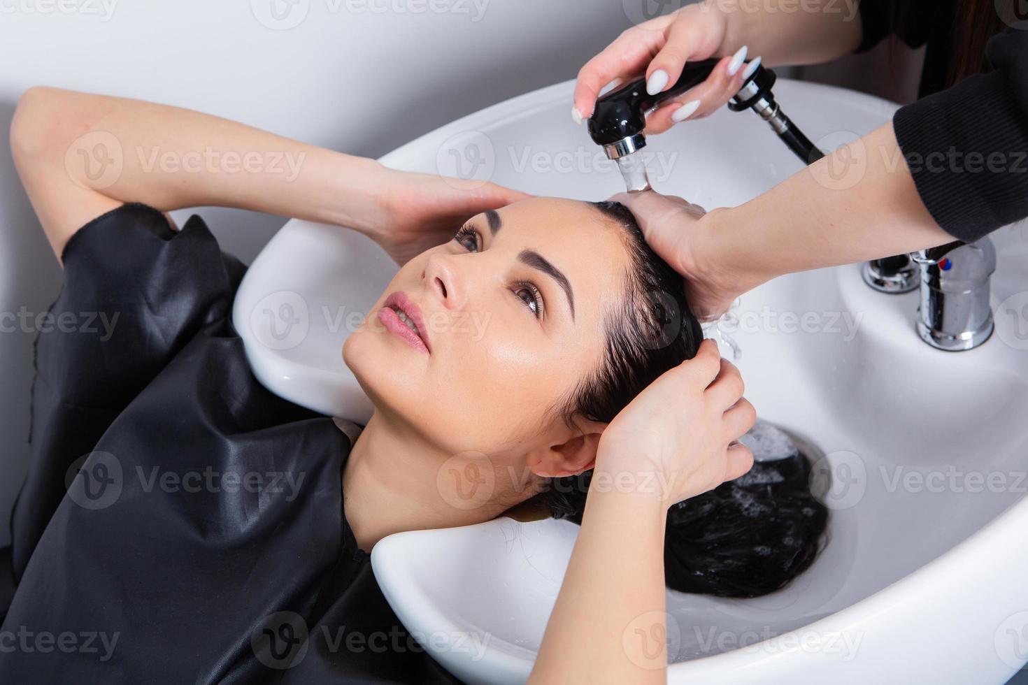 professional hairdresser washing hair of young woman in beauty salon photo