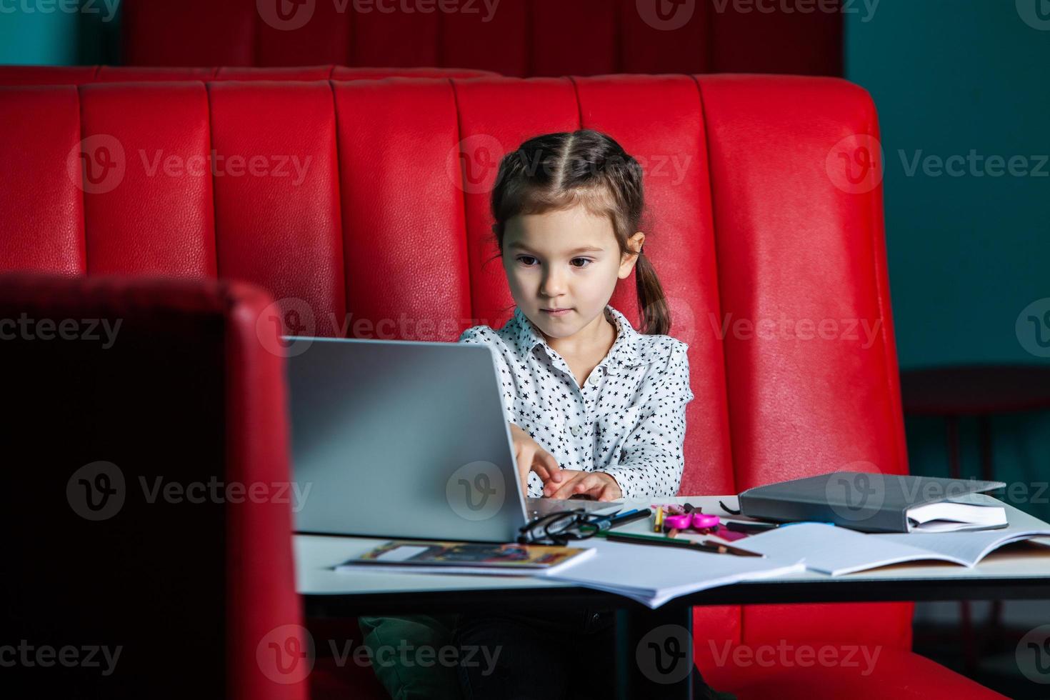 Cute little girl using laptop at home. Back to school concept.  the girl does her homework alone on the laptop photo