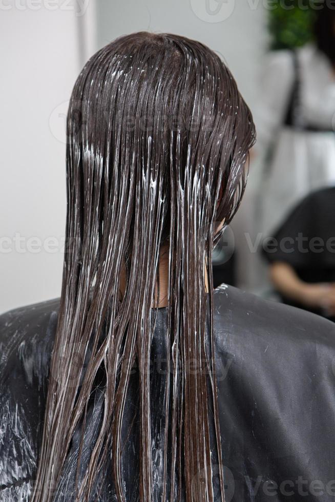 Hairdresser applies a hair mask to straight black hair. Hair care at the beauty salon. photo