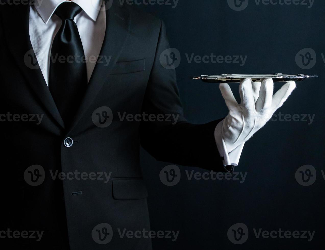 Portrait of Butler or Waiter in Black Suit and White Gloves Holding Serving Tray. Concept of Service Industry and Elegant Hospitality. photo