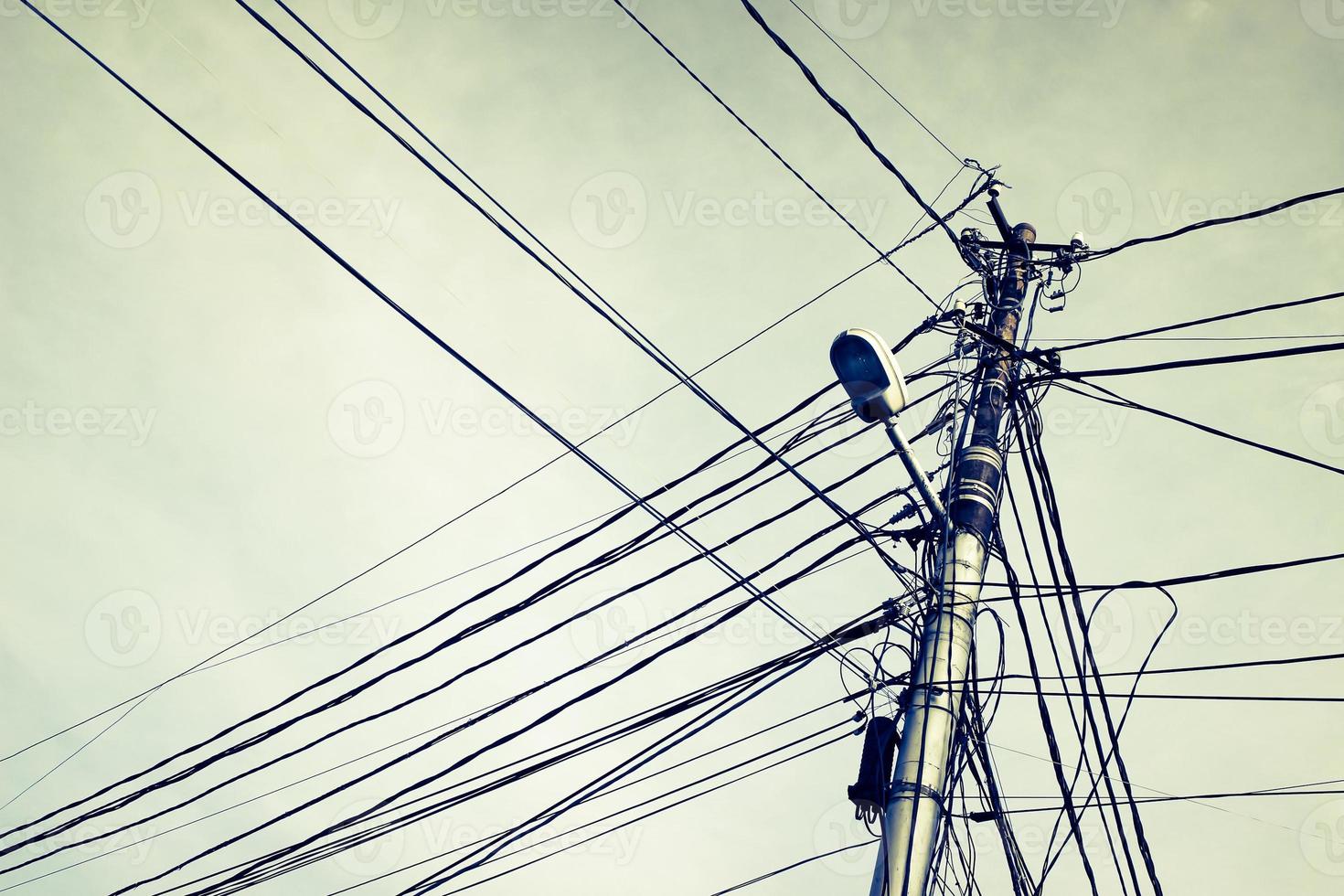 Electricity pylon with street lamp and many cables. photo