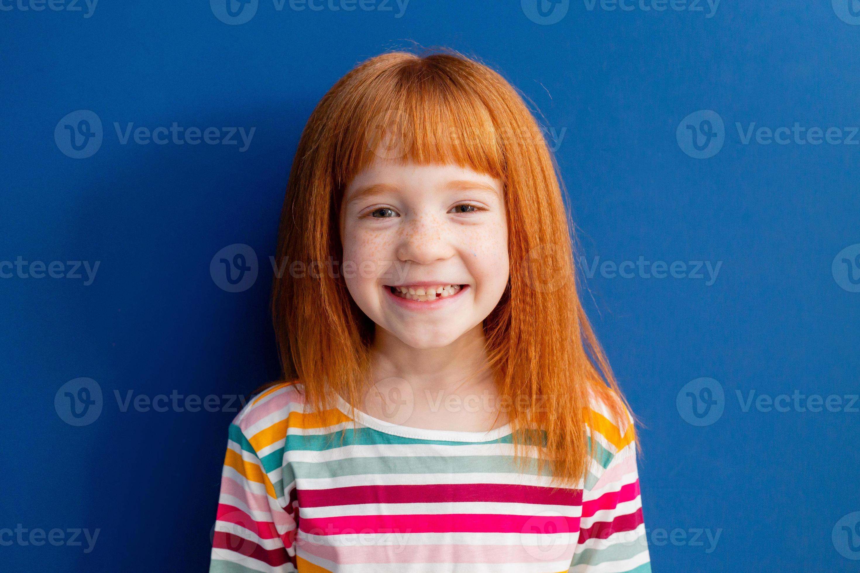 little girl with red hair in a multicolored smile stands on a blue