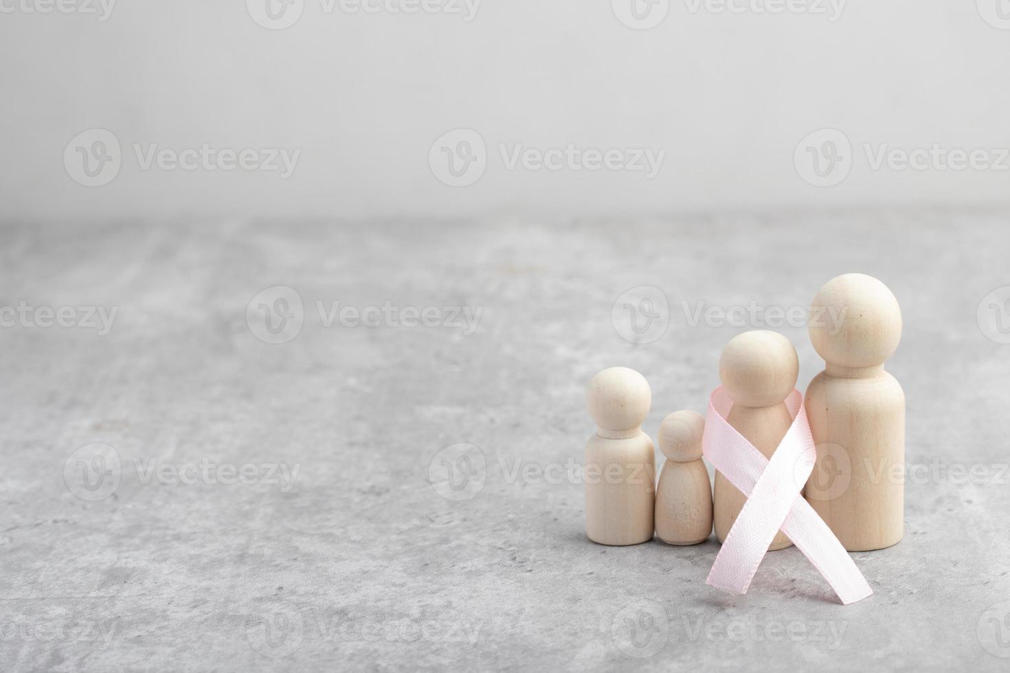 figura familiar de madera y cinta rosa. concepto de tratamiento del cáncer. foto