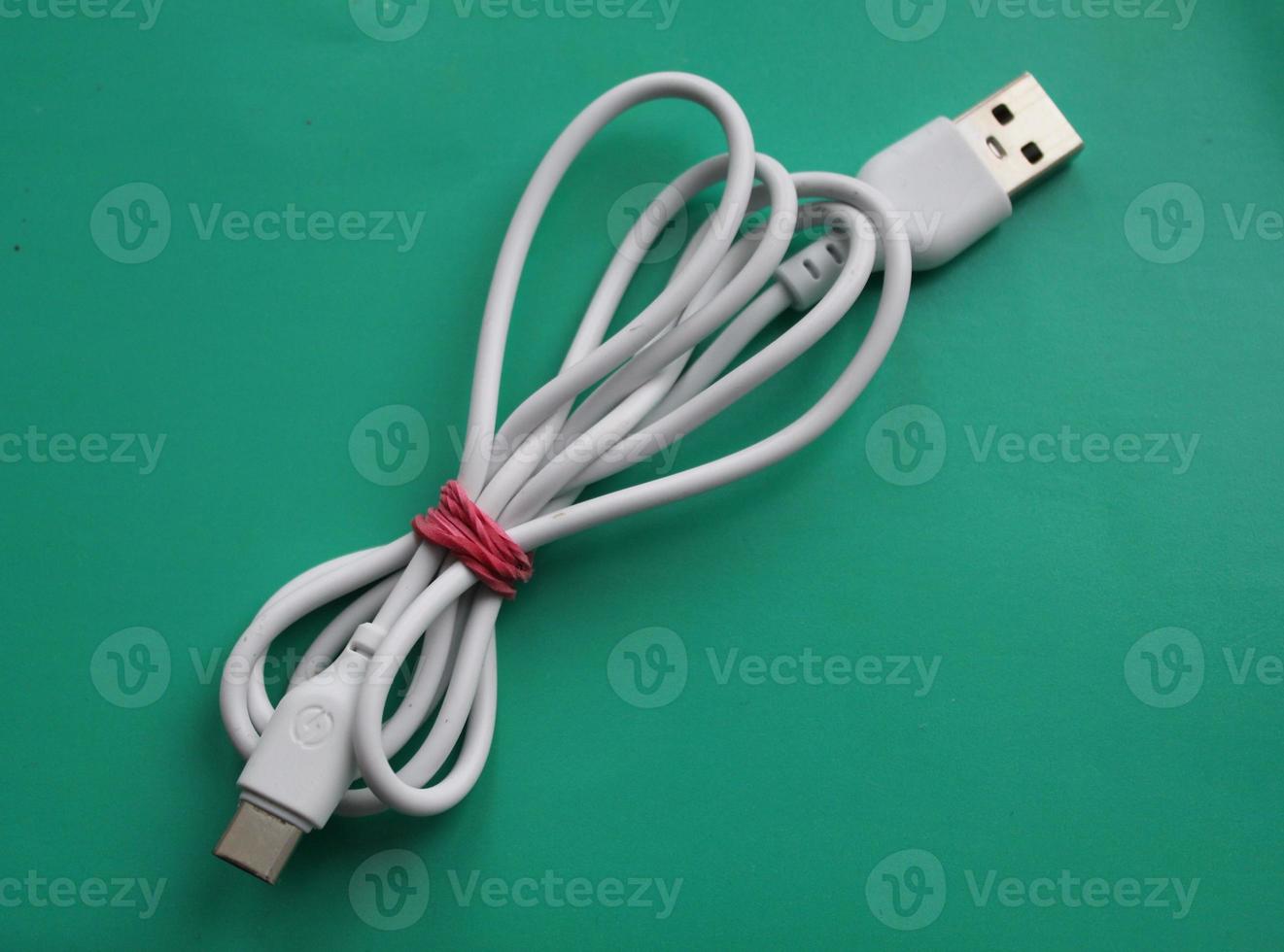 un cable micro usb blanco, tiene una forma ancha y plana para transferir datos y cargar baterías de teléfonos inteligentes. ilustración de un rollo de un cable micro usb en una mesa de madera. foto