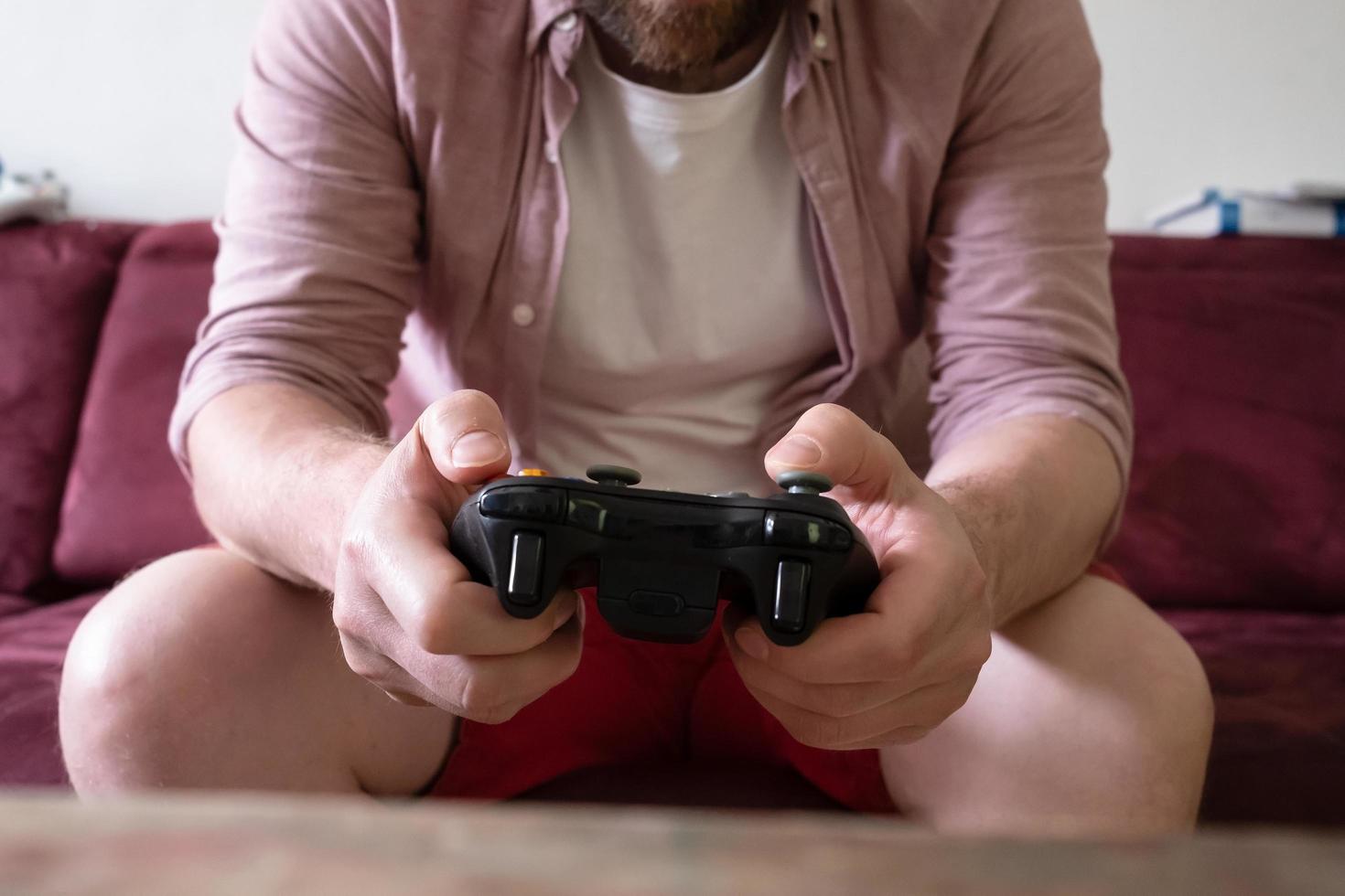 hands with gamepad of man sitting on sofa and playing video games photo