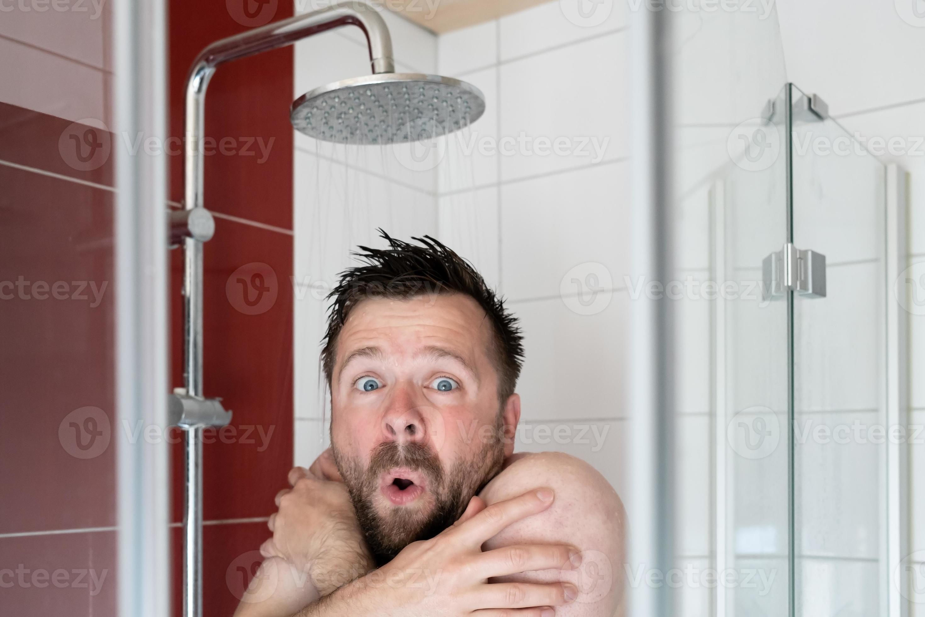 Man in the shower under cold water, he freezes and looks miserable