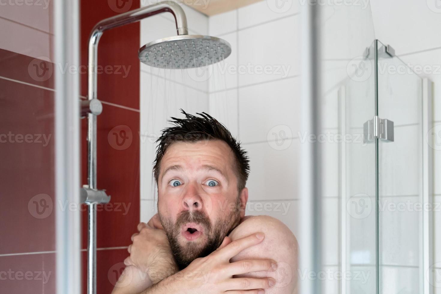 Man in the shower under cold water, he freezes and looks miserable. Energy crisis concept