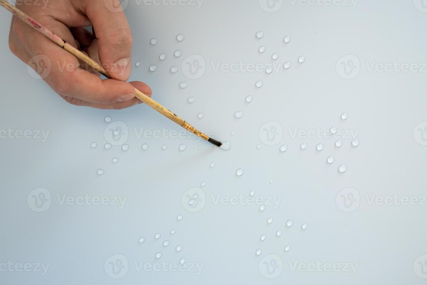 Male hand with a drawing brush draws a snowflake from water drops, on a gray background. Flat lay. Top view. photo