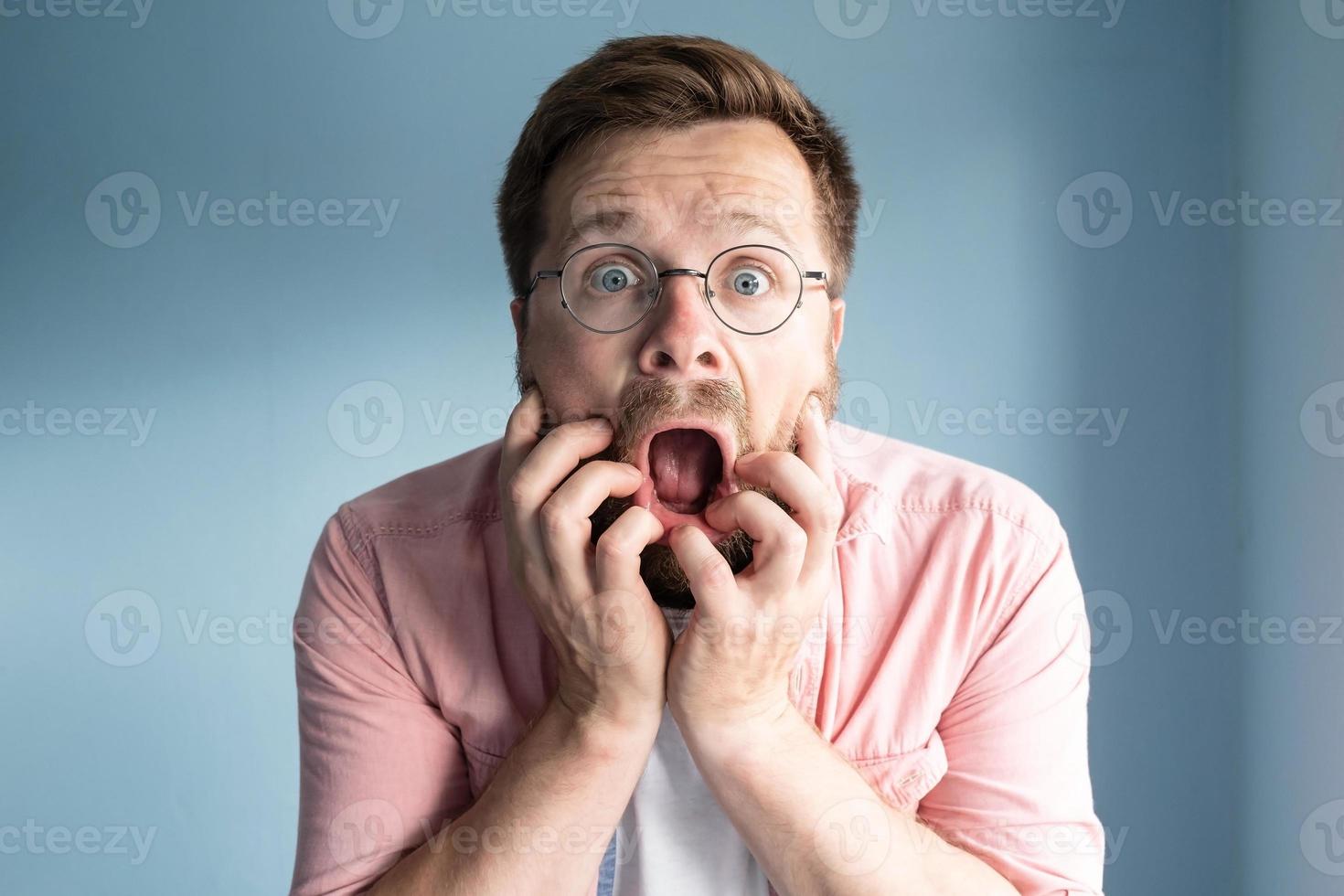 el hombre con anteojos está muy asustado, se lleva las manos a la cara, abre la boca en estado de shock y mira con ojos grandes. foto