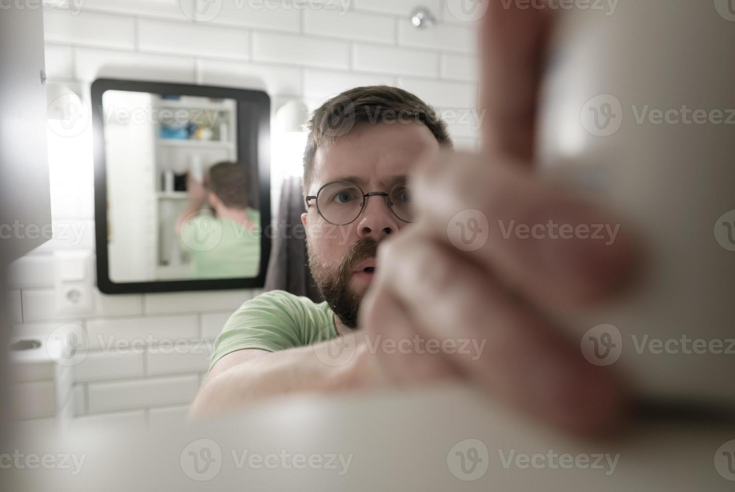 View of the cabinet from the inside and a man who wants to take something from it, against the background of a mirror in the bathroom. photo