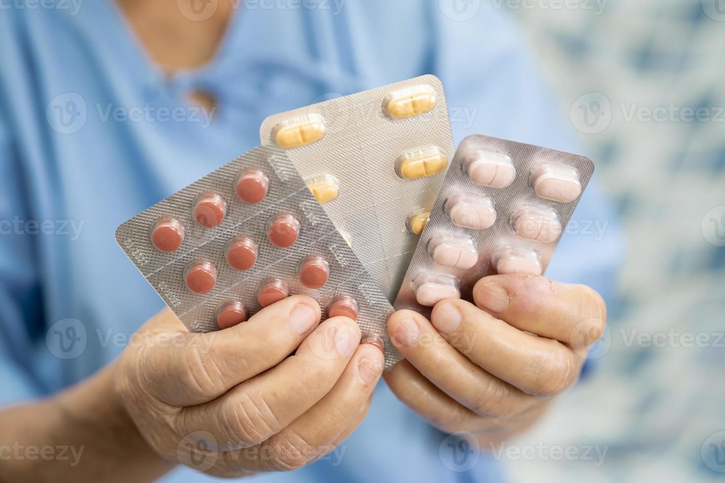 Asian senior or elderly old lady woman patient holding antibiotics capsule pills in blister packaging for treatment infection patient in hospital, Pharmacy drugstore concept. photo